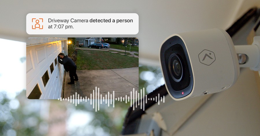 A home security camera with an image of a person peering into a driveway. “Driveway Camera detected a person at 7:07 pm.” 
