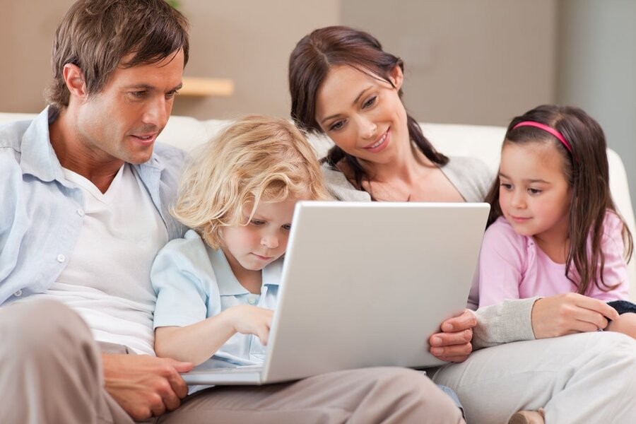 A family of four using a laptop together while sitting on a couch.