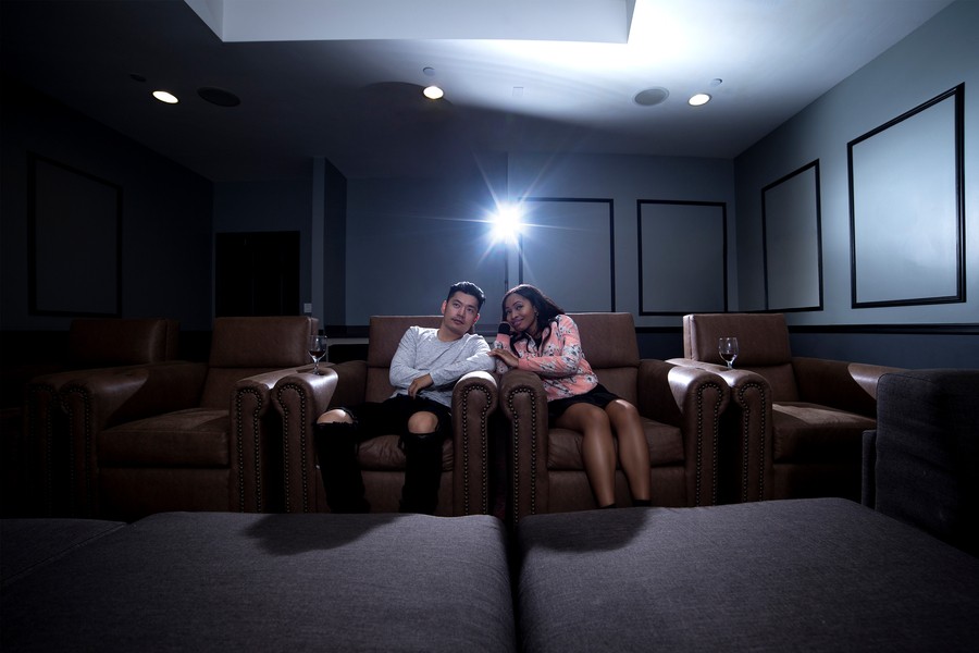 A couple watching  movie in a home theater with a projector behind them.