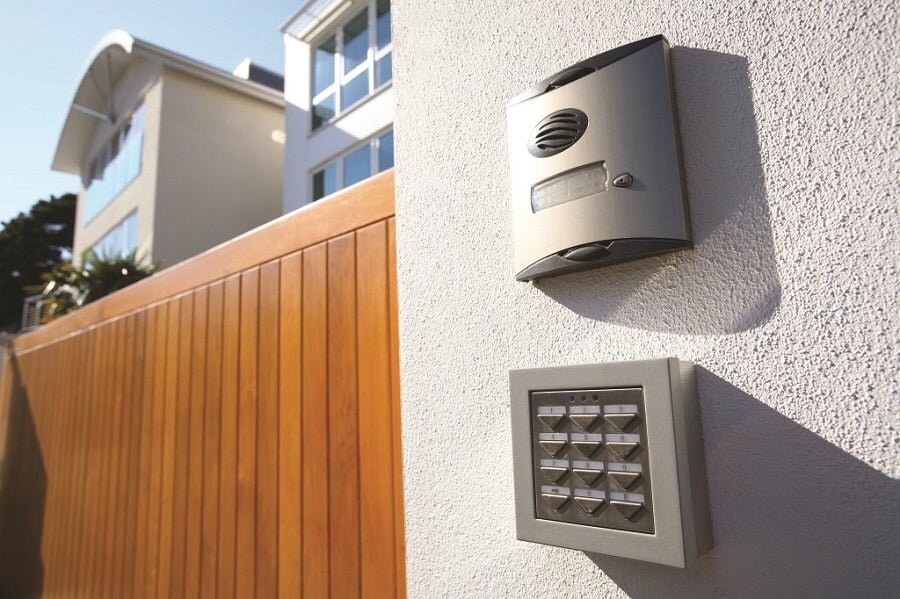 A home’s exterior showing a fence and a smart security system’s alarm and panel on the side of the wall.