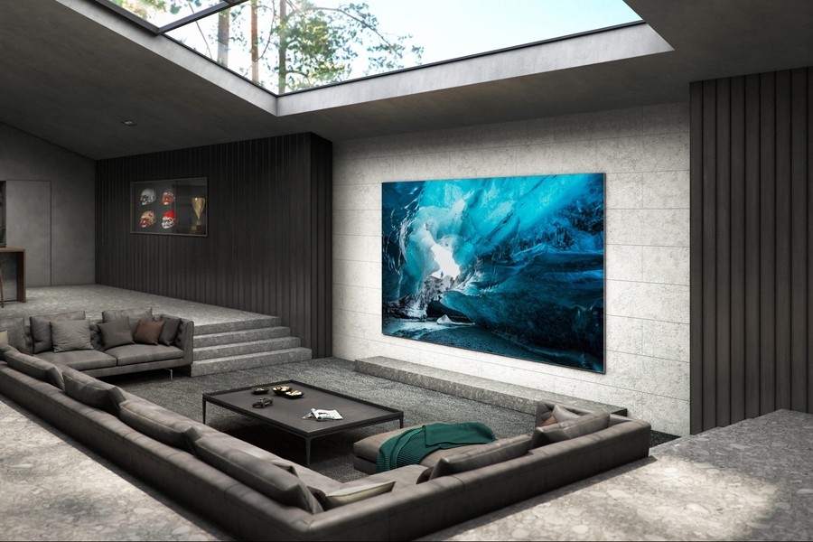 Modern home theater room featuring a large high-resolution TV mounted on a stone wall, with comfortable sectional sofas and natural light streaming from a skylight above. 